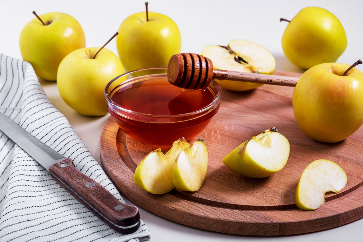 תפוחים שלמים וחתוכים על מגש עץ עם קערית דבש