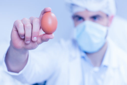 איש בחלוק מעבדה ומסכה מחזיק ביצה
